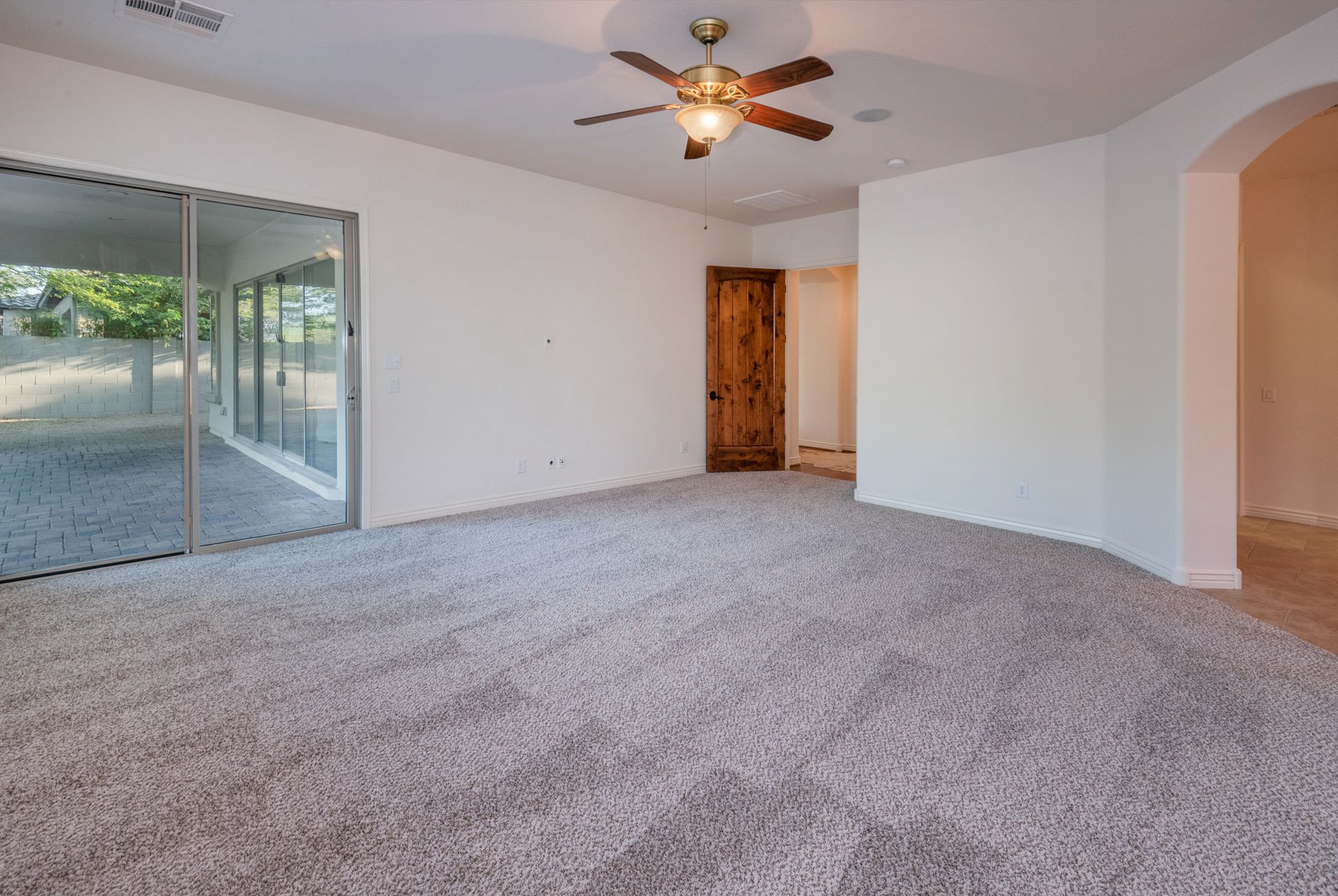 An empty living room with a ceiling fan and sliding glass doors.