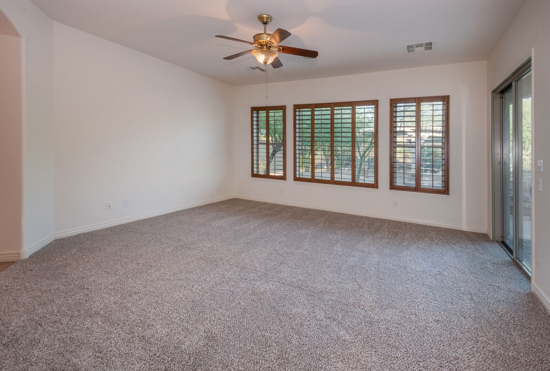 An empty living room with a ceiling fan and lots of windows