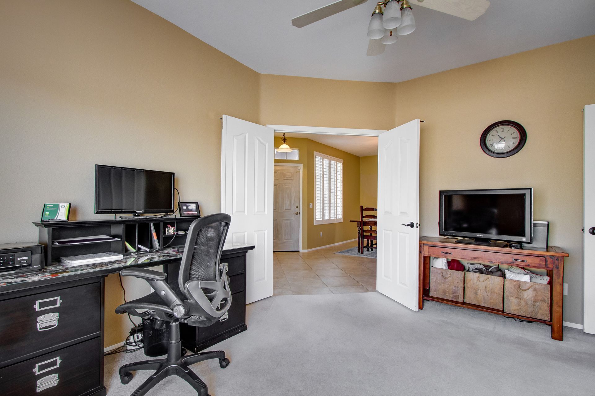 A bedroom with a desk , chair , television and a ceiling fan.