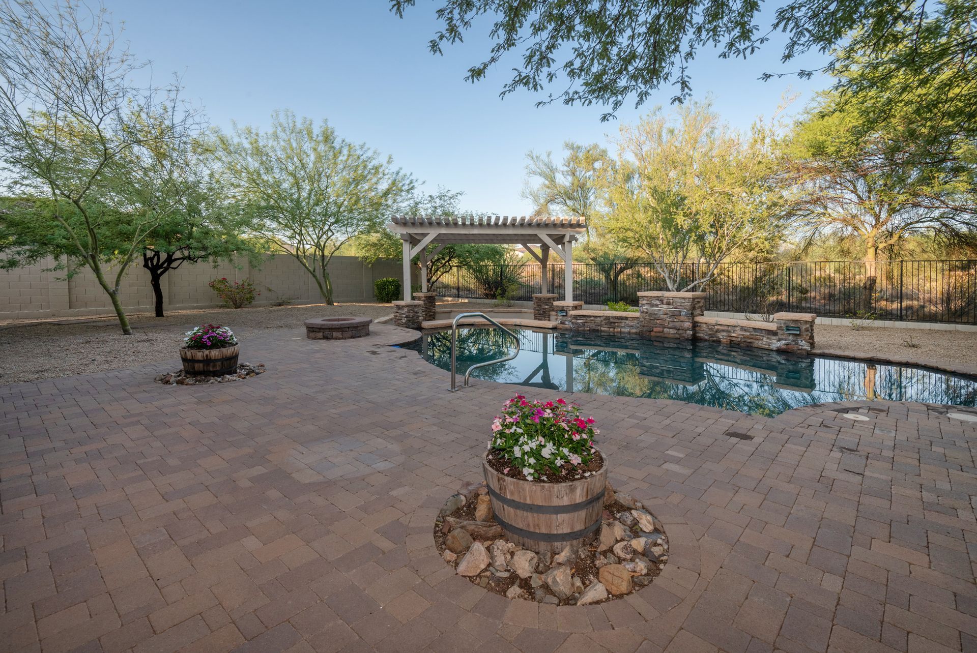 A large swimming pool is surrounded by a brick patio and a pergola.