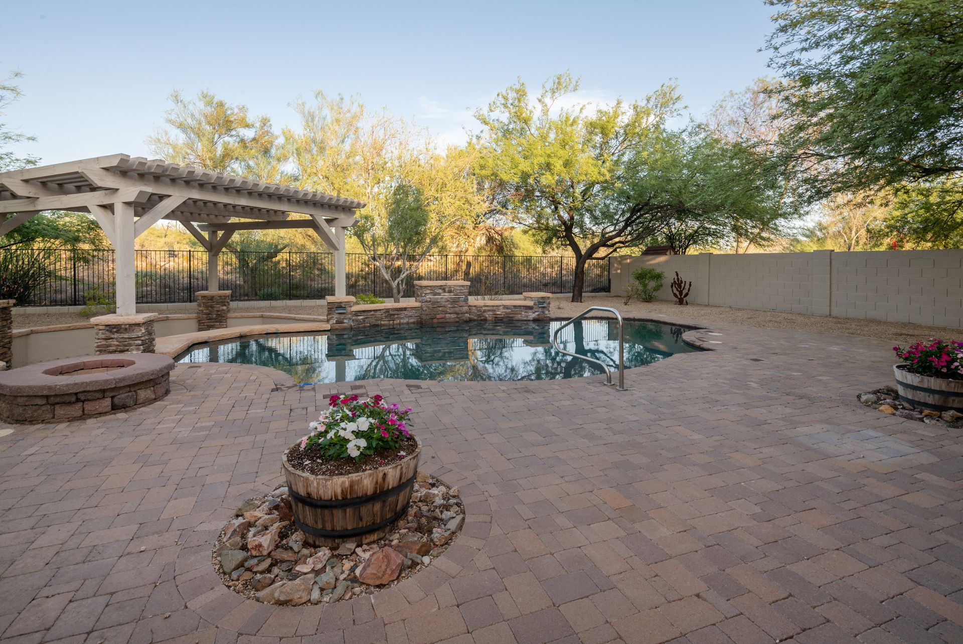 A large swimming pool is surrounded by a brick patio and a pergola.