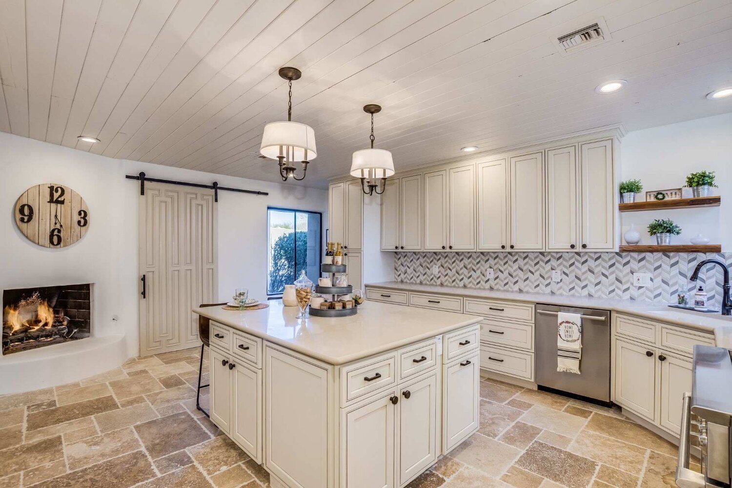 A kitchen with white cabinets , stainless steel appliances , a large island and a fireplace.