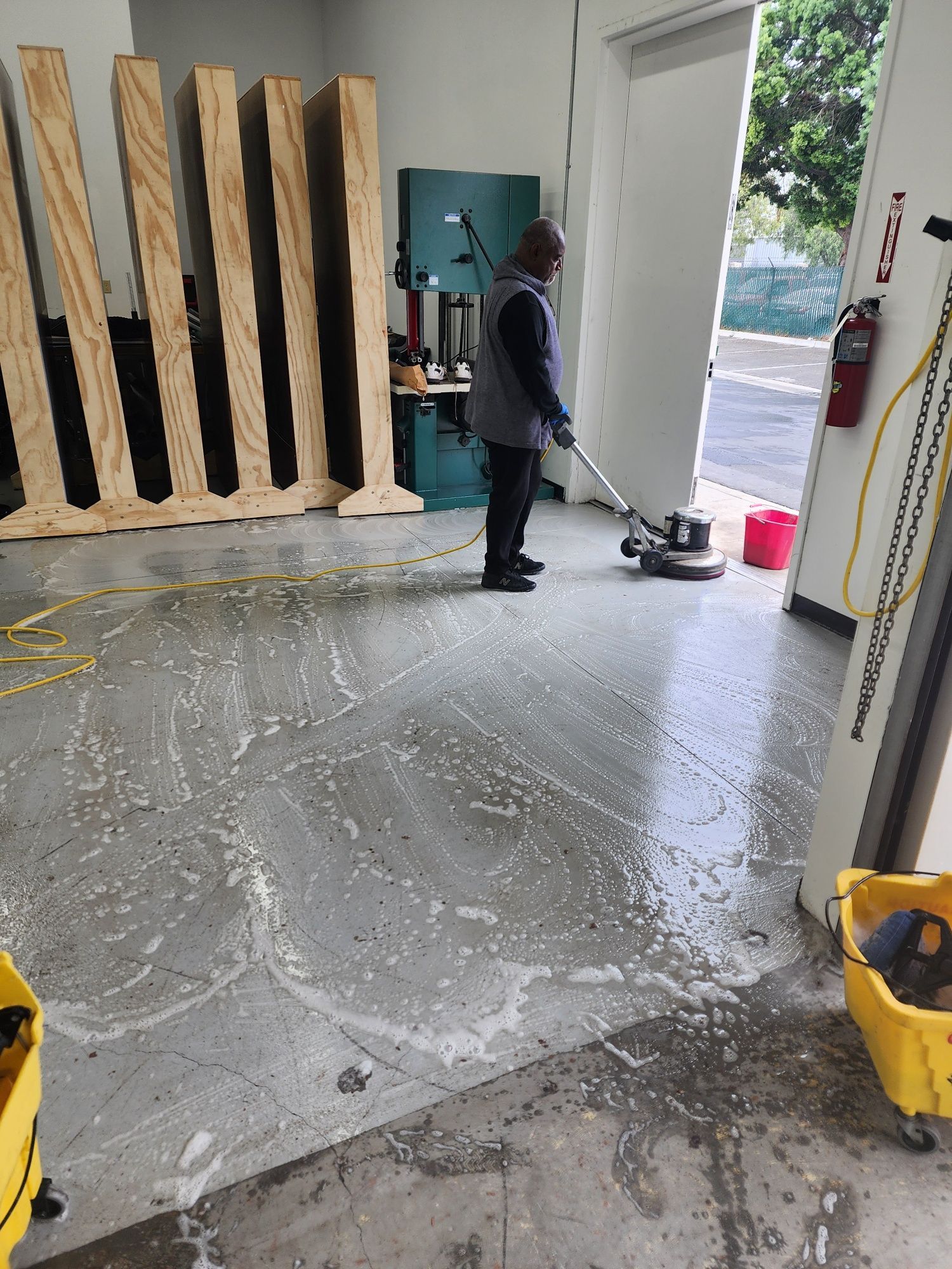 A person cleaning a concrete floor with a floor buffer in a workshop or storage area.