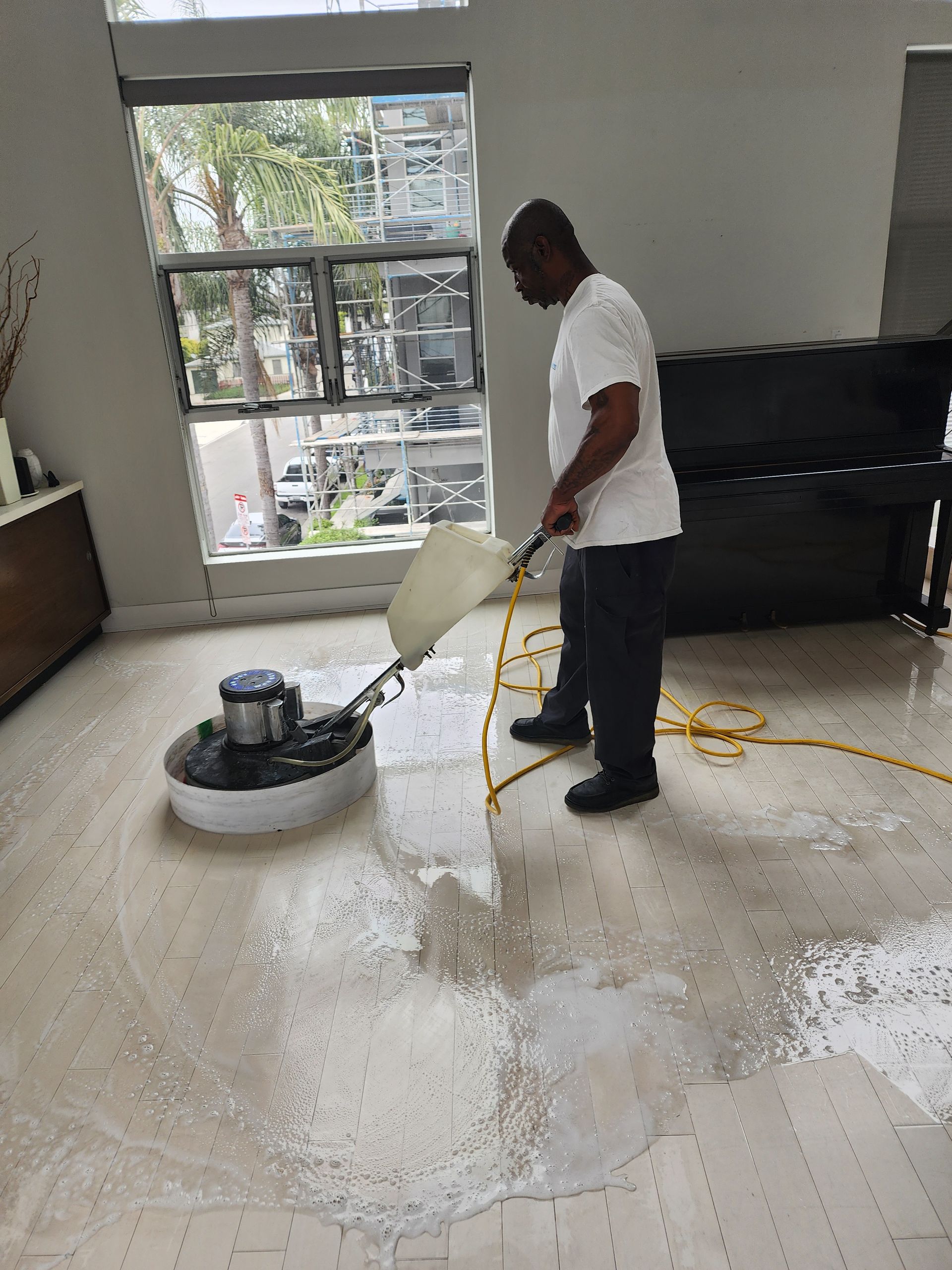 Person using a floor buffer to clean a white tiled room near large windows.