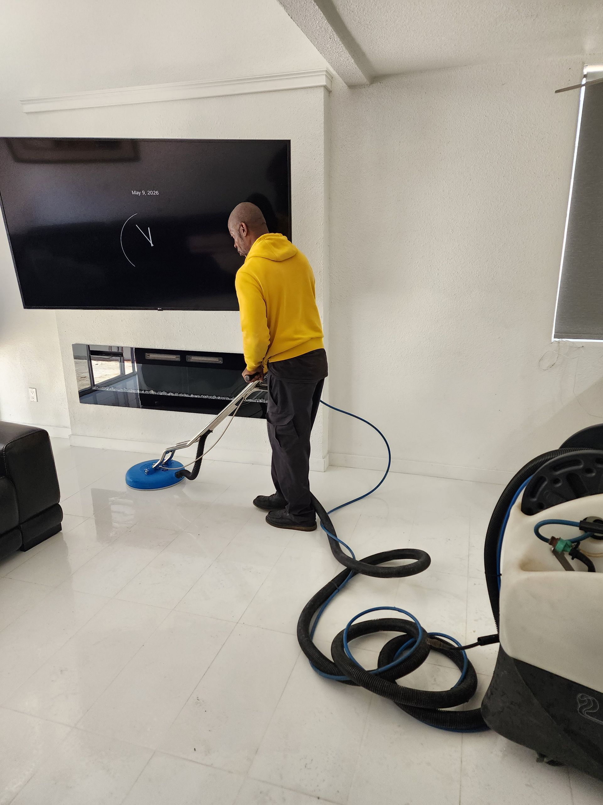 Person in a yellow shirt vacuuming a bright living room with a large wall-mounted TV.