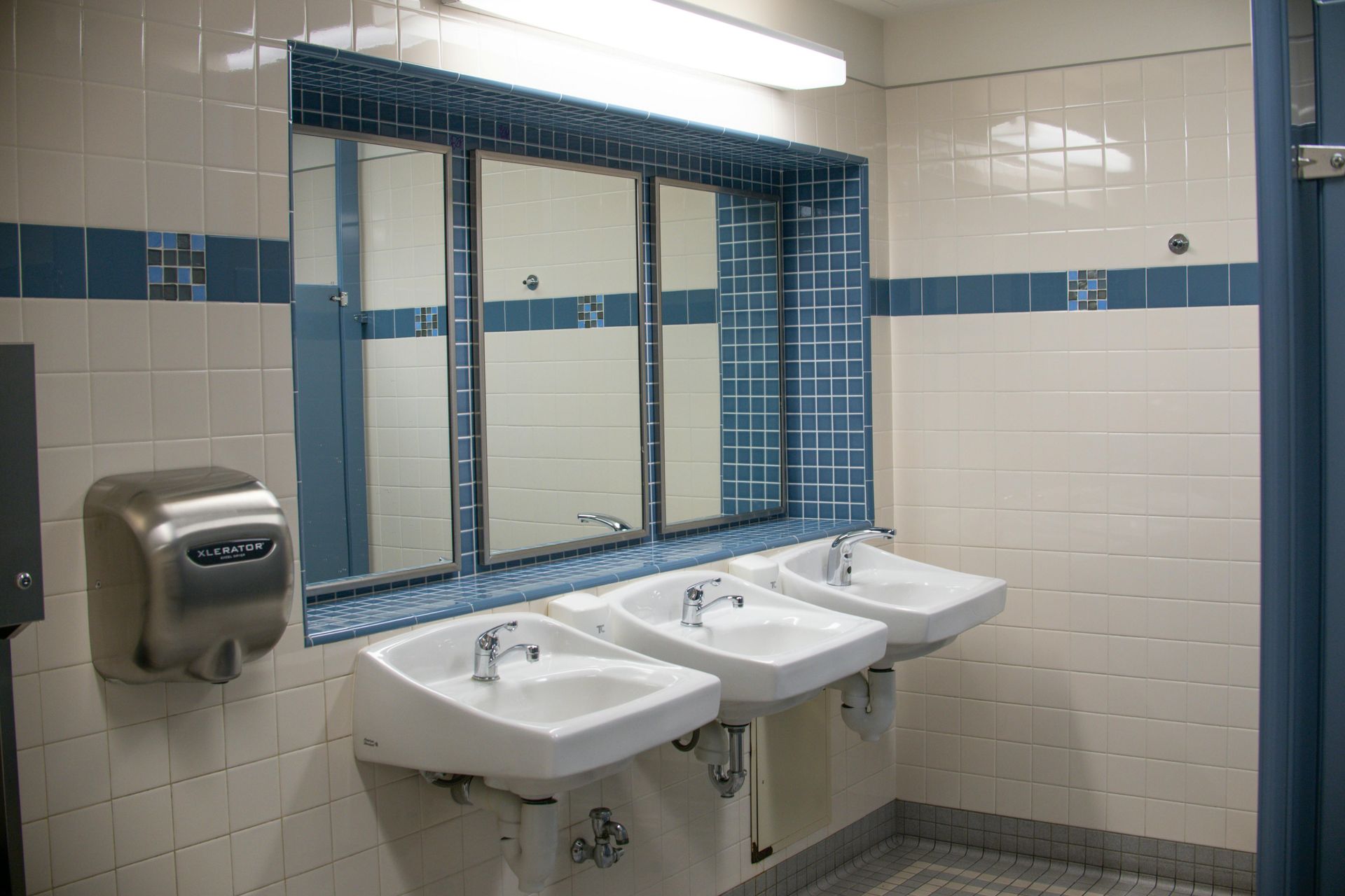 Public restroom with three sinks, mirrors, and white and blue tiled walls.