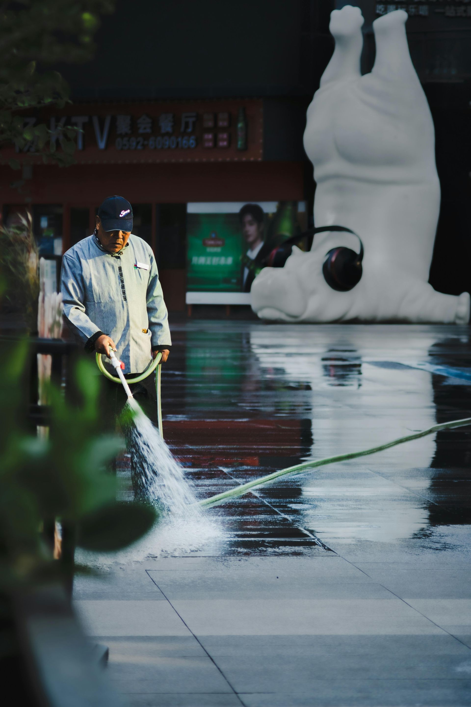 Worker power-washing wet pavement beside a large white inflatable sculpture in a city plaza