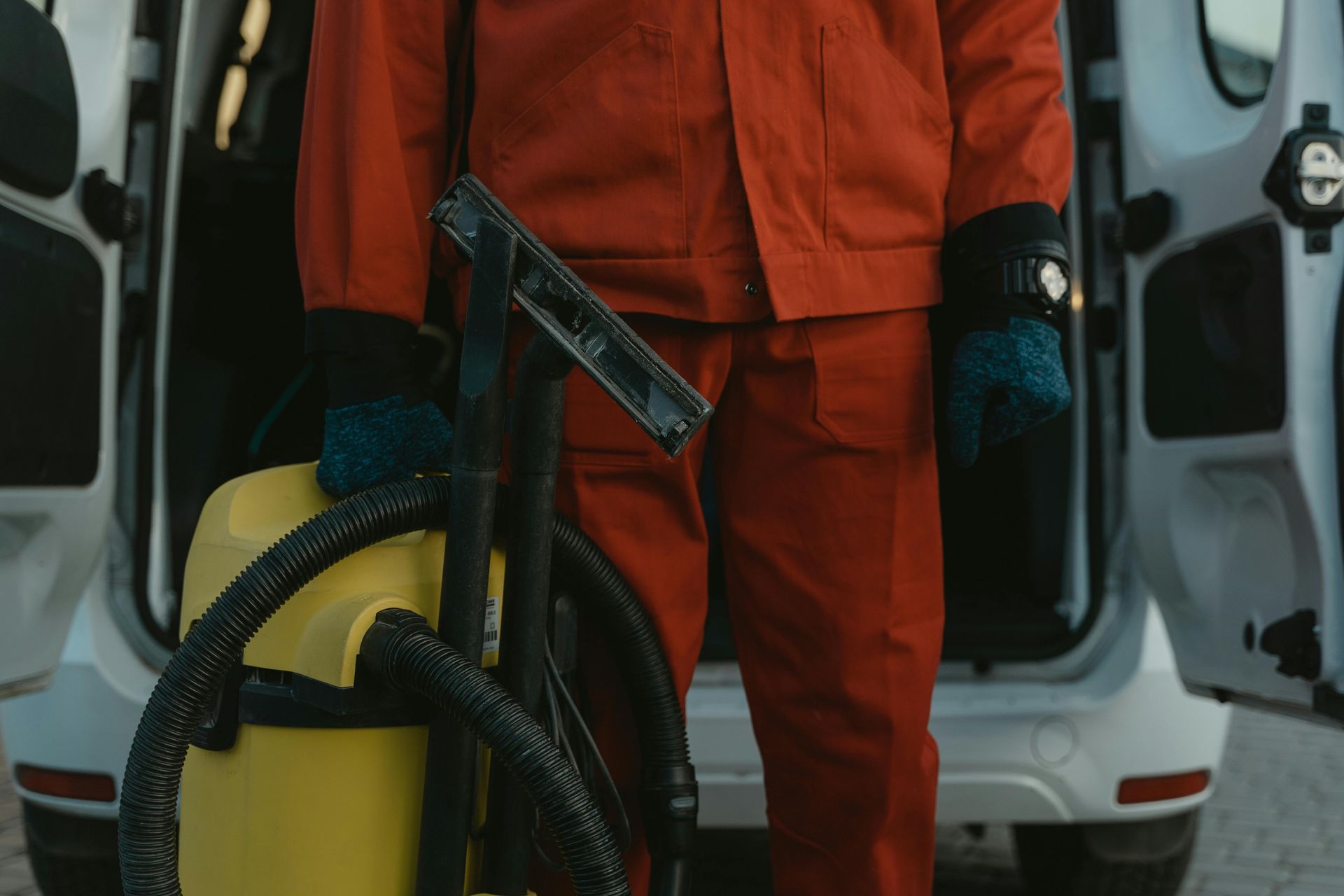 Person in red work suit holding cleaning tools in front of a van.