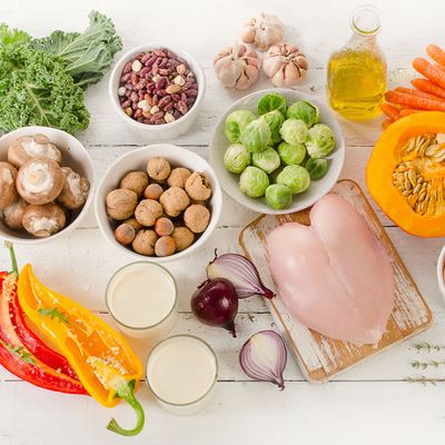 Verschiedene frische Gemüsesorten, Pilze, Hühnchen, Bohnen, Öl und Milch auf weißem Hintergrund arrangiert