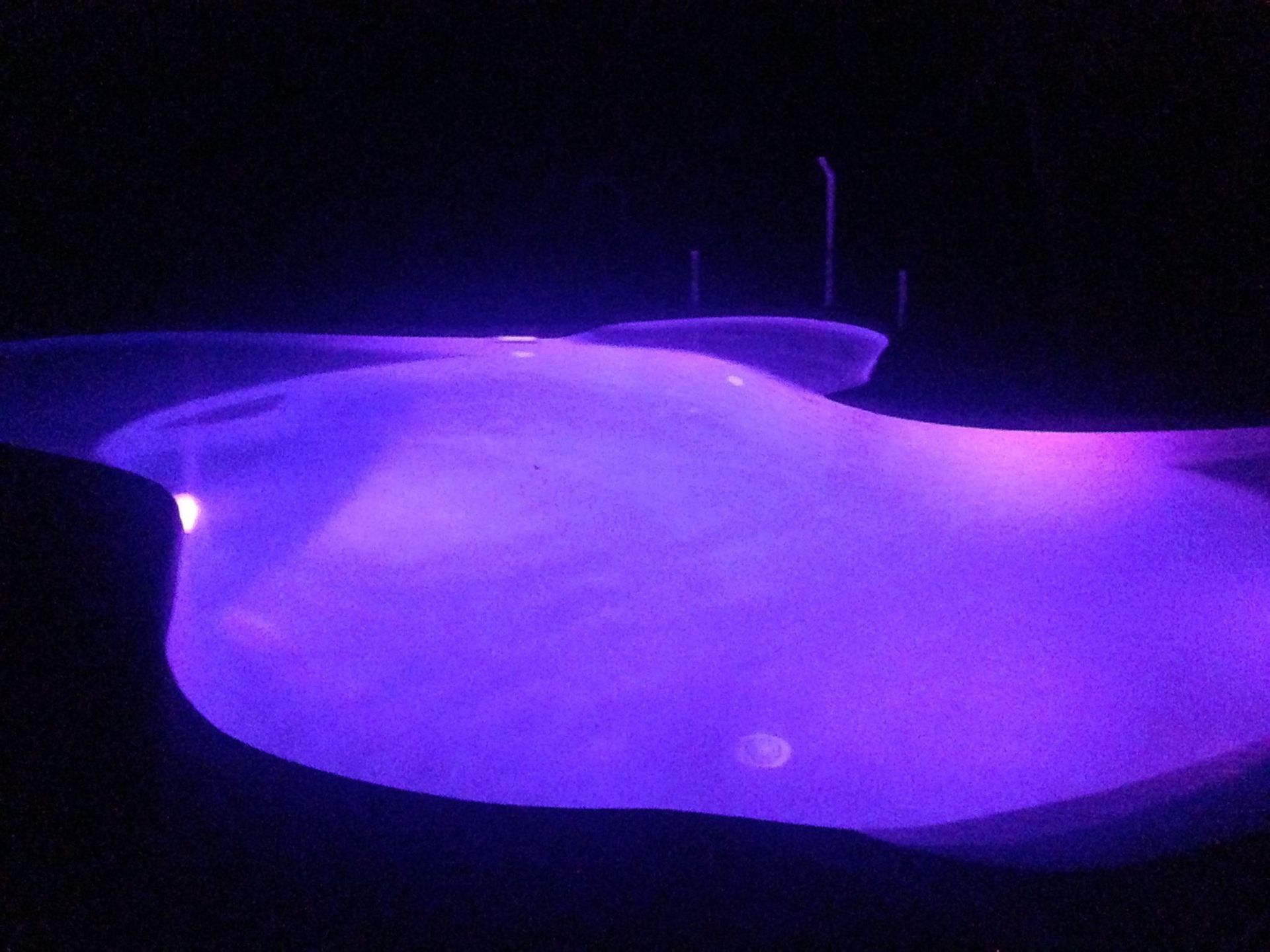A Swimming Pool is Lit Up With Purple Lights at Night — Fannie Bay Pool Shop in Winnellie, NT