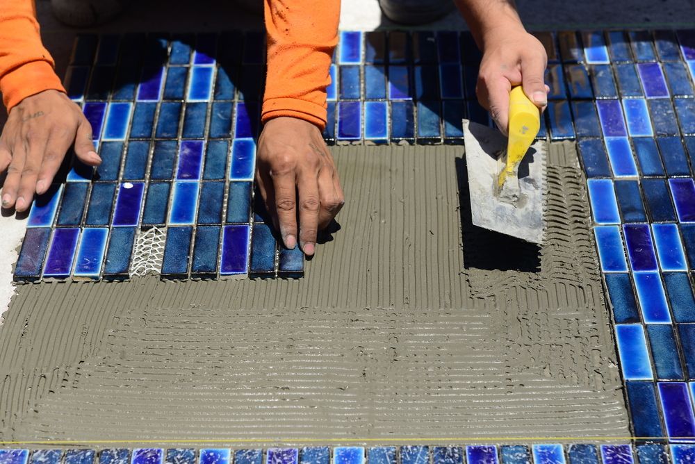 A Man is Laying Tiles on the Floor With a Trowel — Fannie Bay Pool Shop in Winnellie, NT