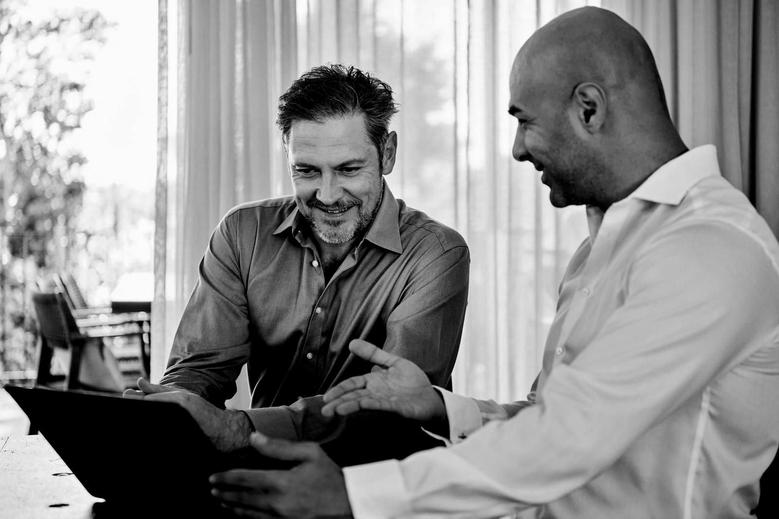 Two men are sitting at a table looking at a tablet.