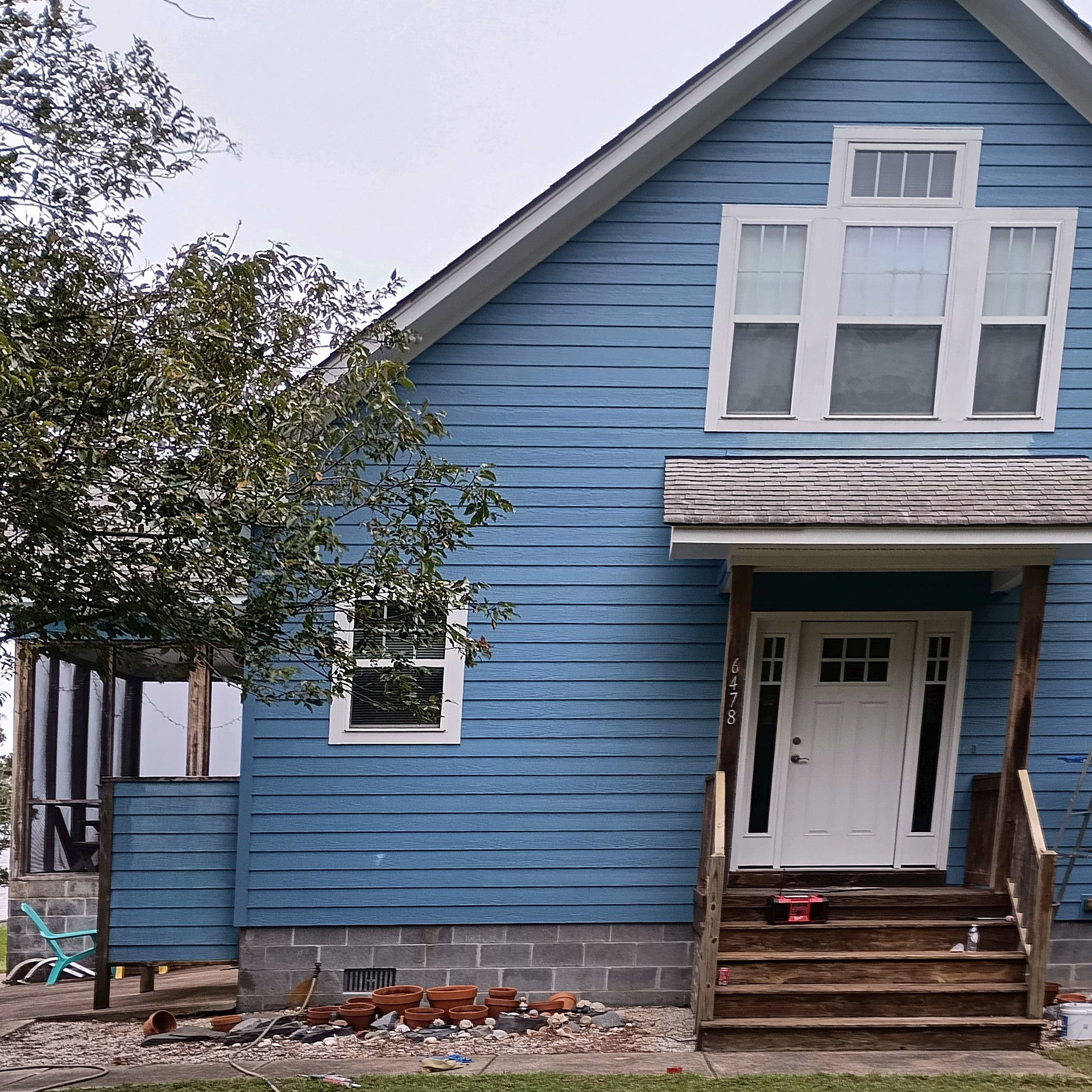 Blue house with white trim, brown steps, and a small tree.