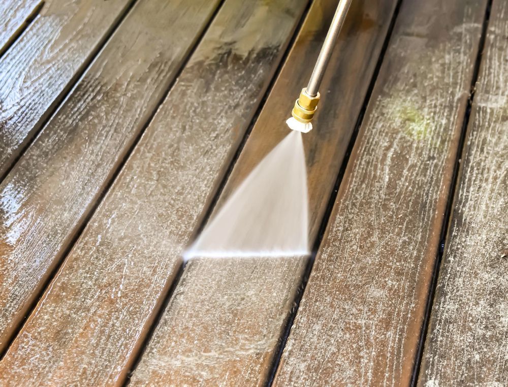 A person is using a high pressure washer to clean a wooden deck.