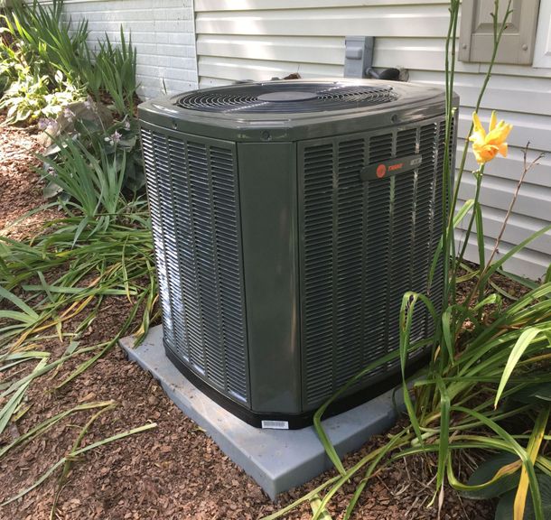 An air conditioner is sitting on top of a concrete base in front of a house.