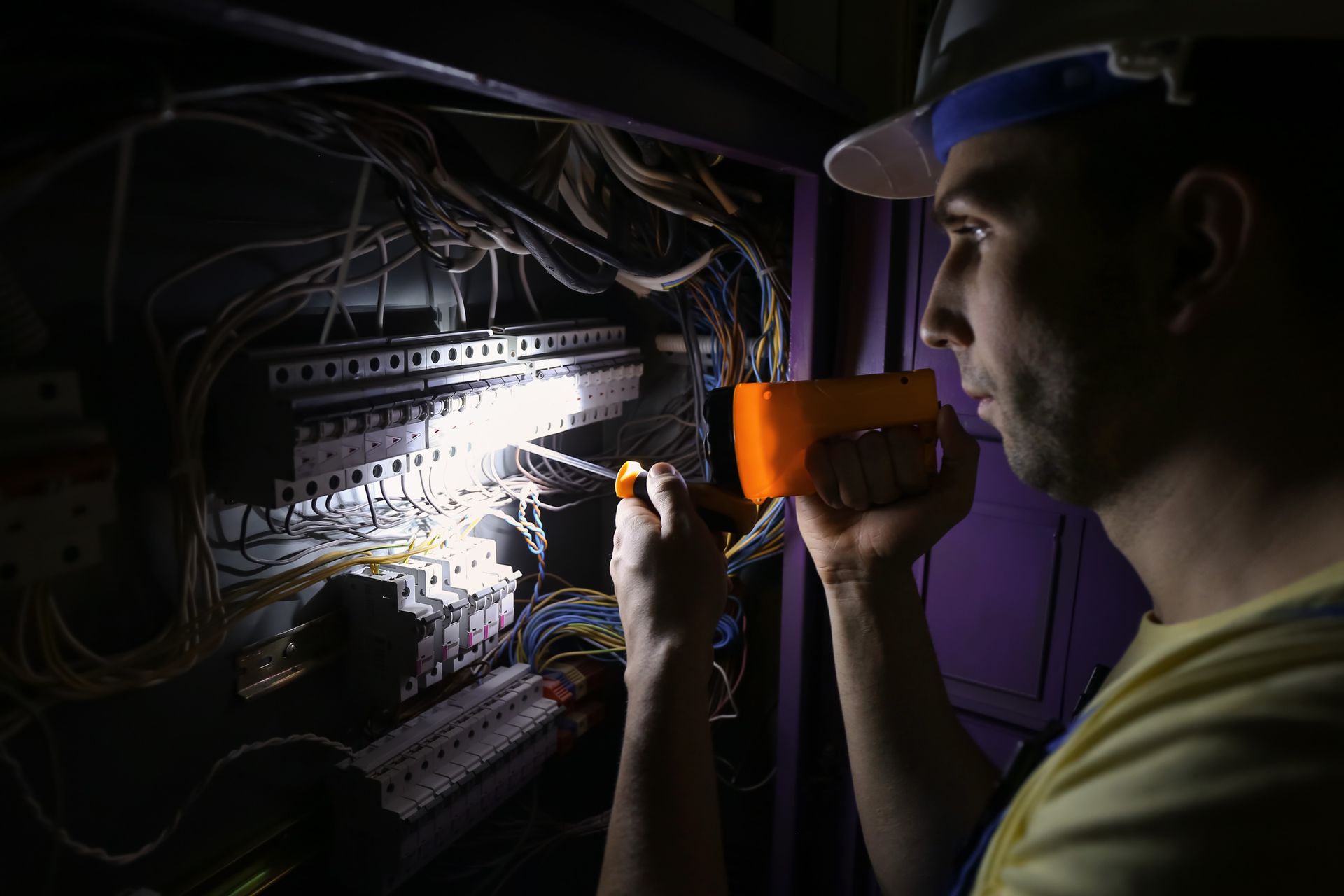 A man is working on an electrical box with a flashlight.