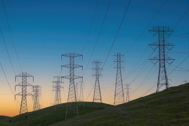 A row of power lines on top of a hill at sunset.
