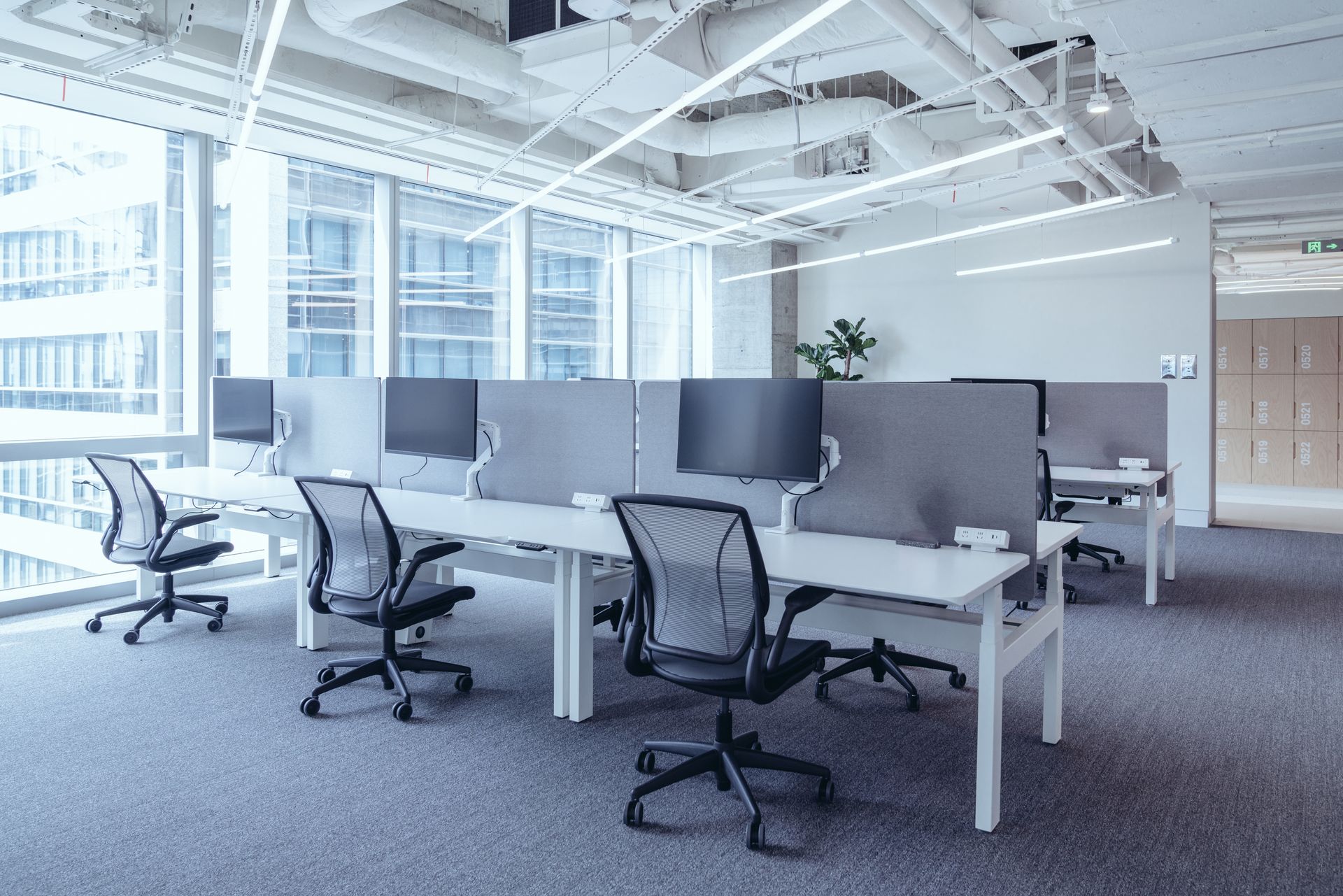 A row of desks and chairs in an office with a lot of windows.