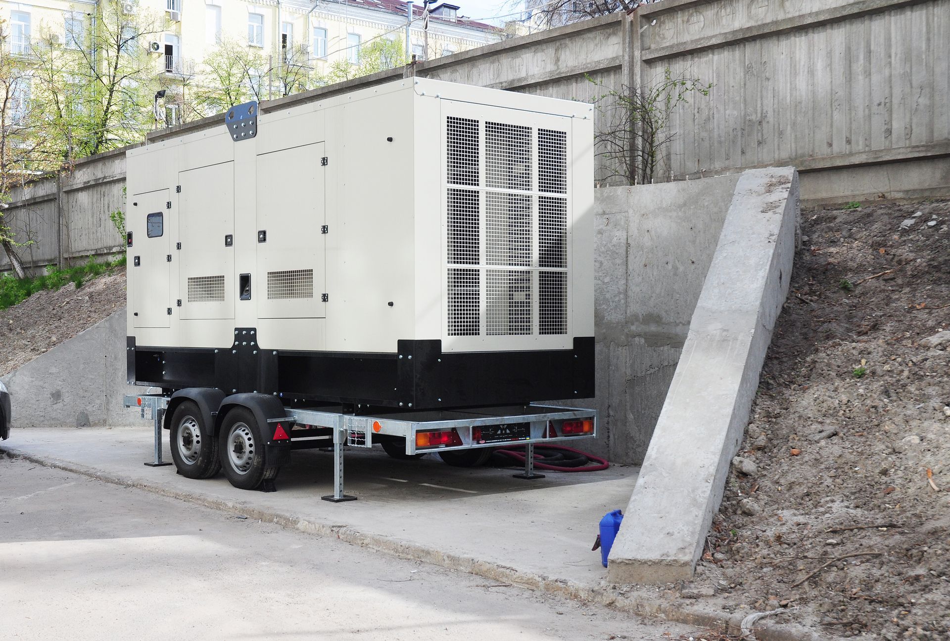 A large generator is parked on a trailer next to a concrete wall.