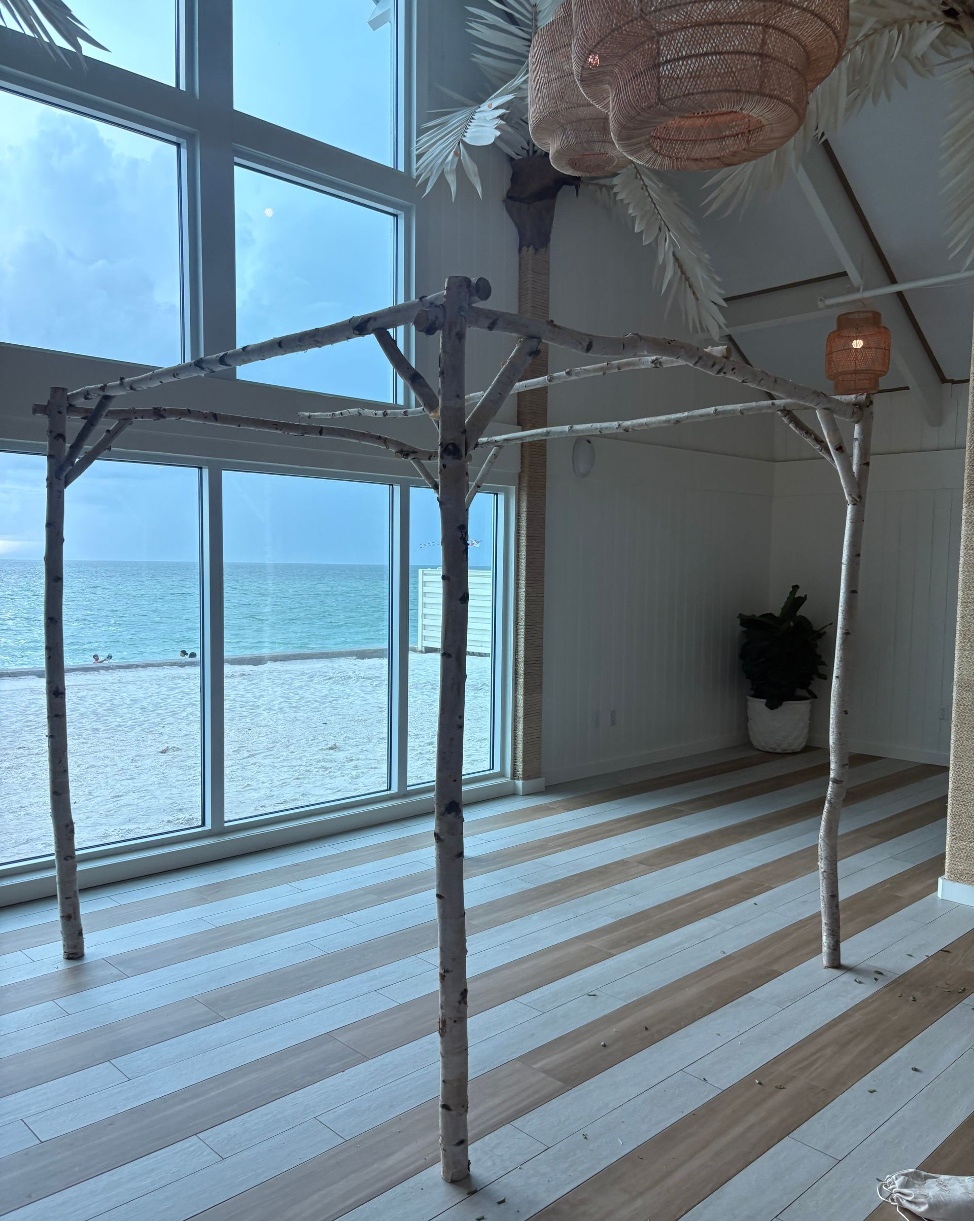 Interior view: beachside room with natural wood posts, striped floor, and ocean view.