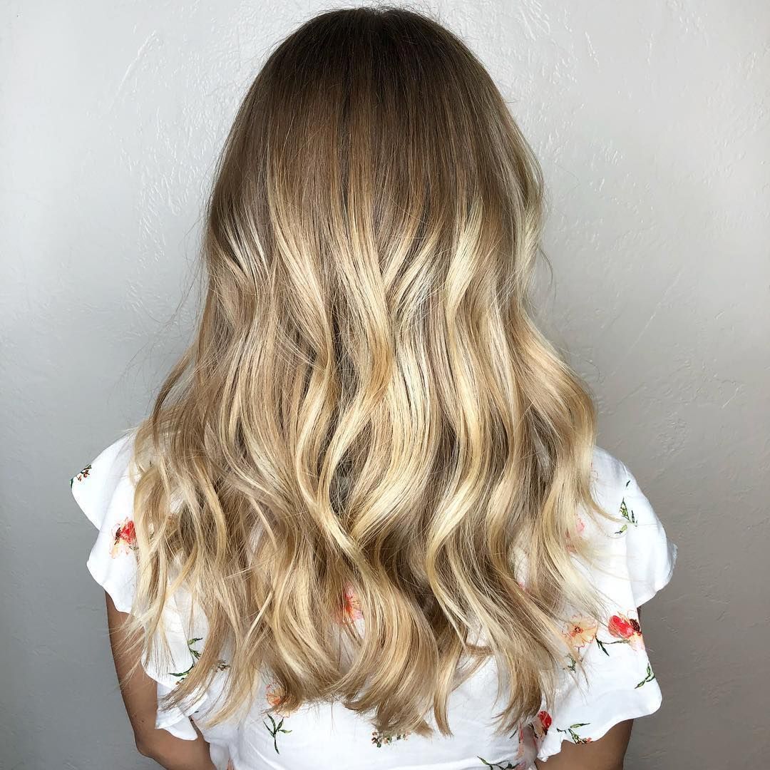 Back view of long, blonde wavy hair with crimped texture, worn by someone in a white floral top against a plain wall.