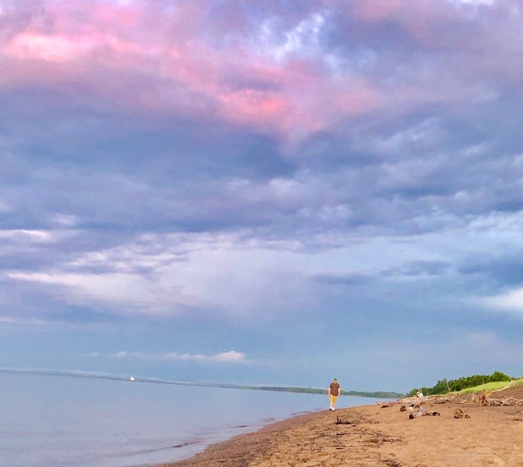 A person is walking along a beach with a pink sky in the background.