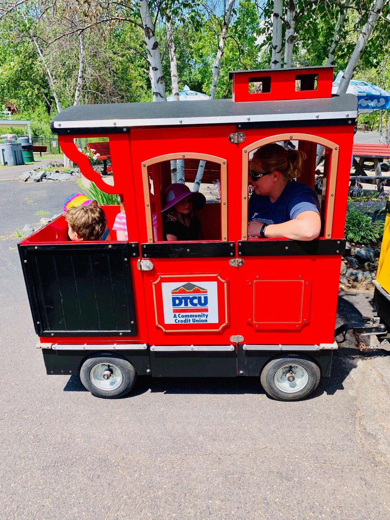 A woman and two children are riding a red train.