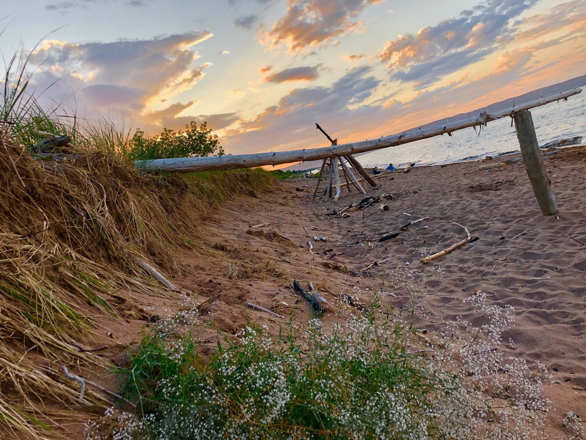 A wooden railing on a sandy beach with a sunset in the background.