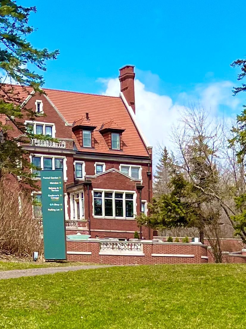Glensheen Mansion with a red tile roof is surrounded by trees and grass.