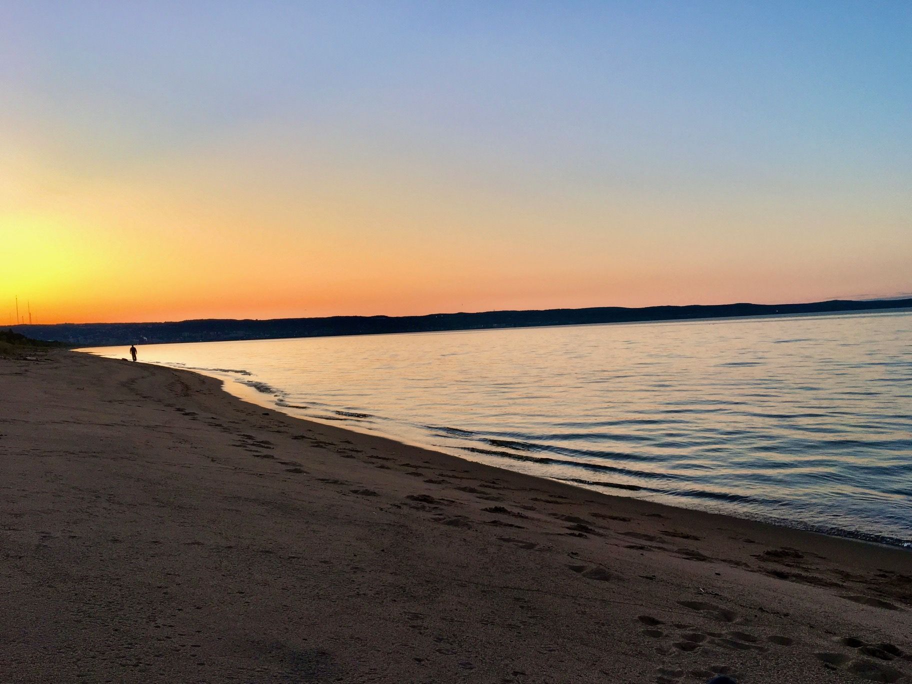 A sunset over a body of water with a sandy beach in the foreground.