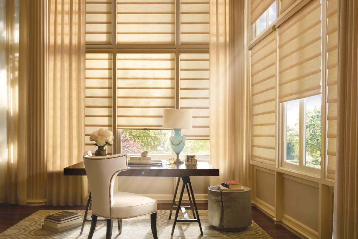 Partly drawn Hunter Douglas Vignette® Roman Shades near a wooden desk.