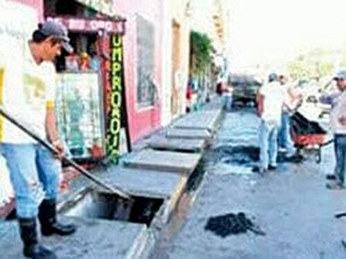 Un grupo de personas está limpiando una tapa de alcantarilla en una acera.