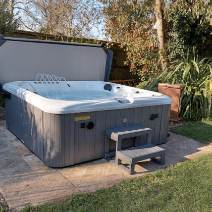 A hot tub is sitting on a patio in a backyard with the lid open.
