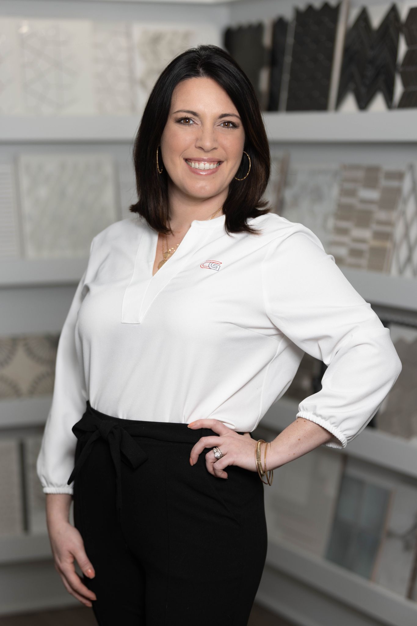 A woman in a white shirt and black pants is standing in front of a display of tiles.