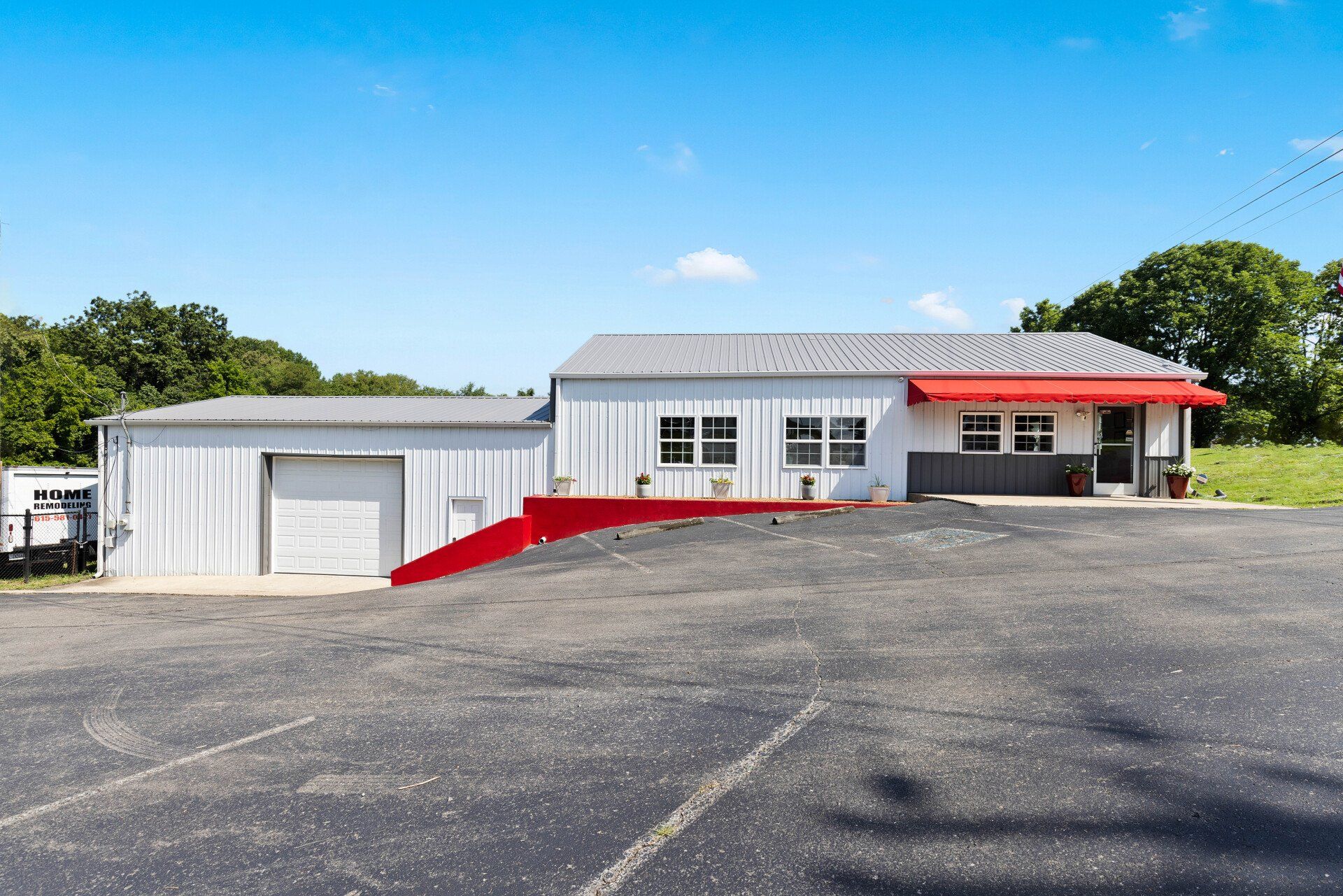A white house with a red awning is sitting in a parking lot.