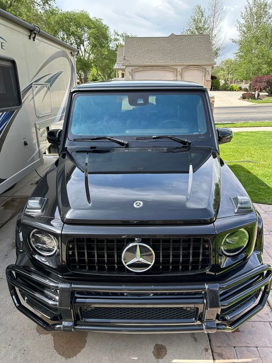 A black mercedes benz g63 amg is parked in a driveway in front of a house.