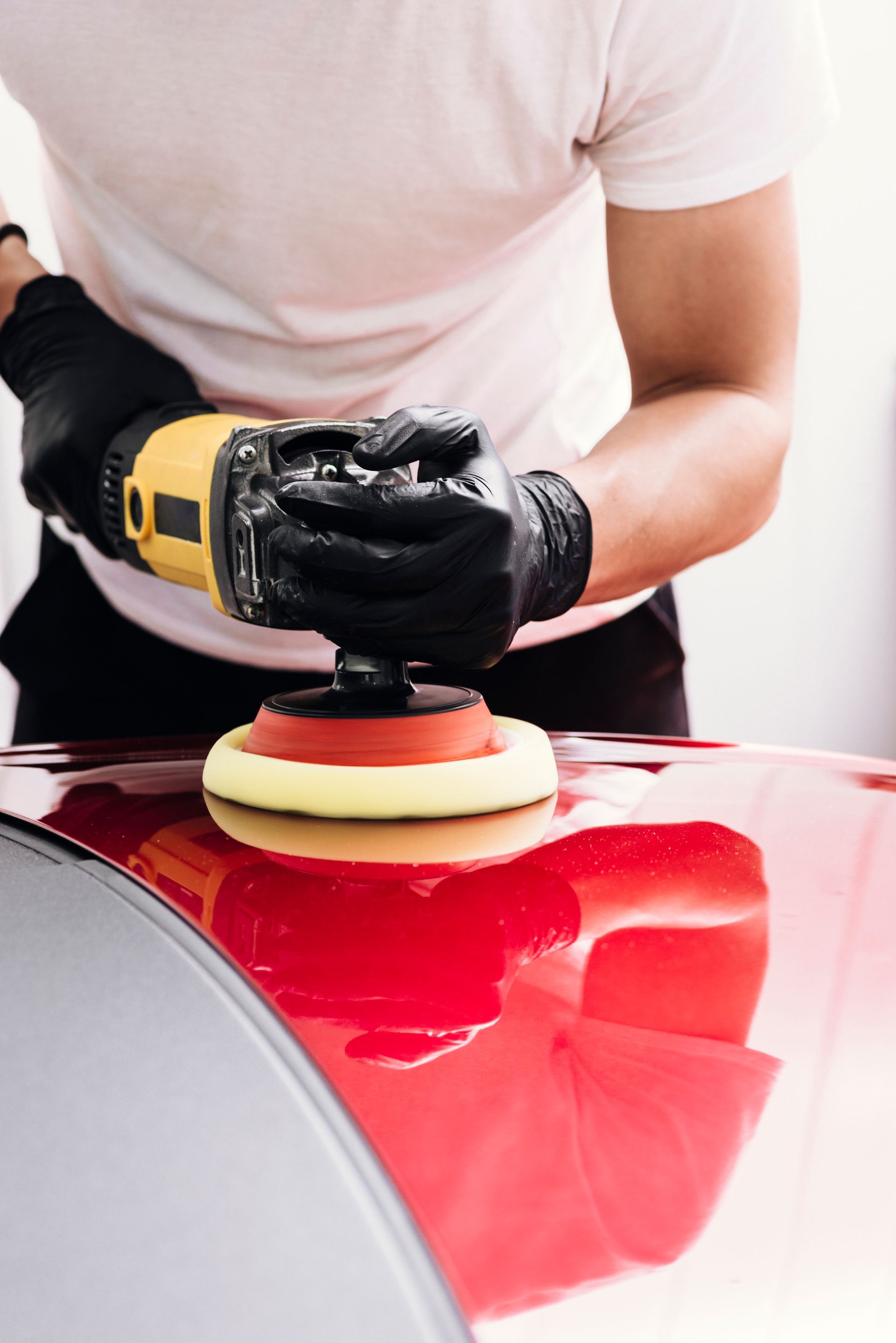 A man is polishing a red car with a machine.