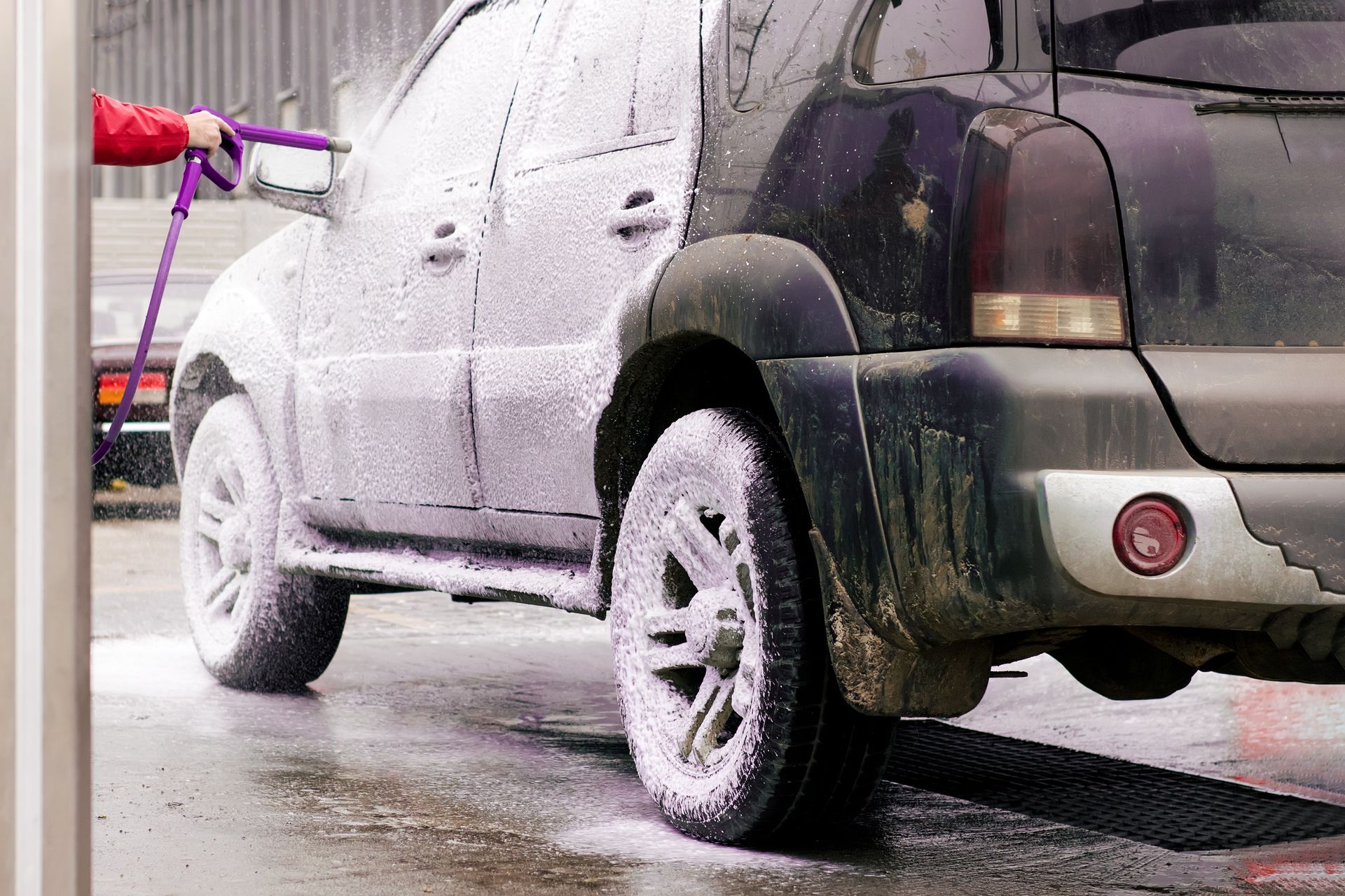 A person is washing a car with a hose at a car wash.