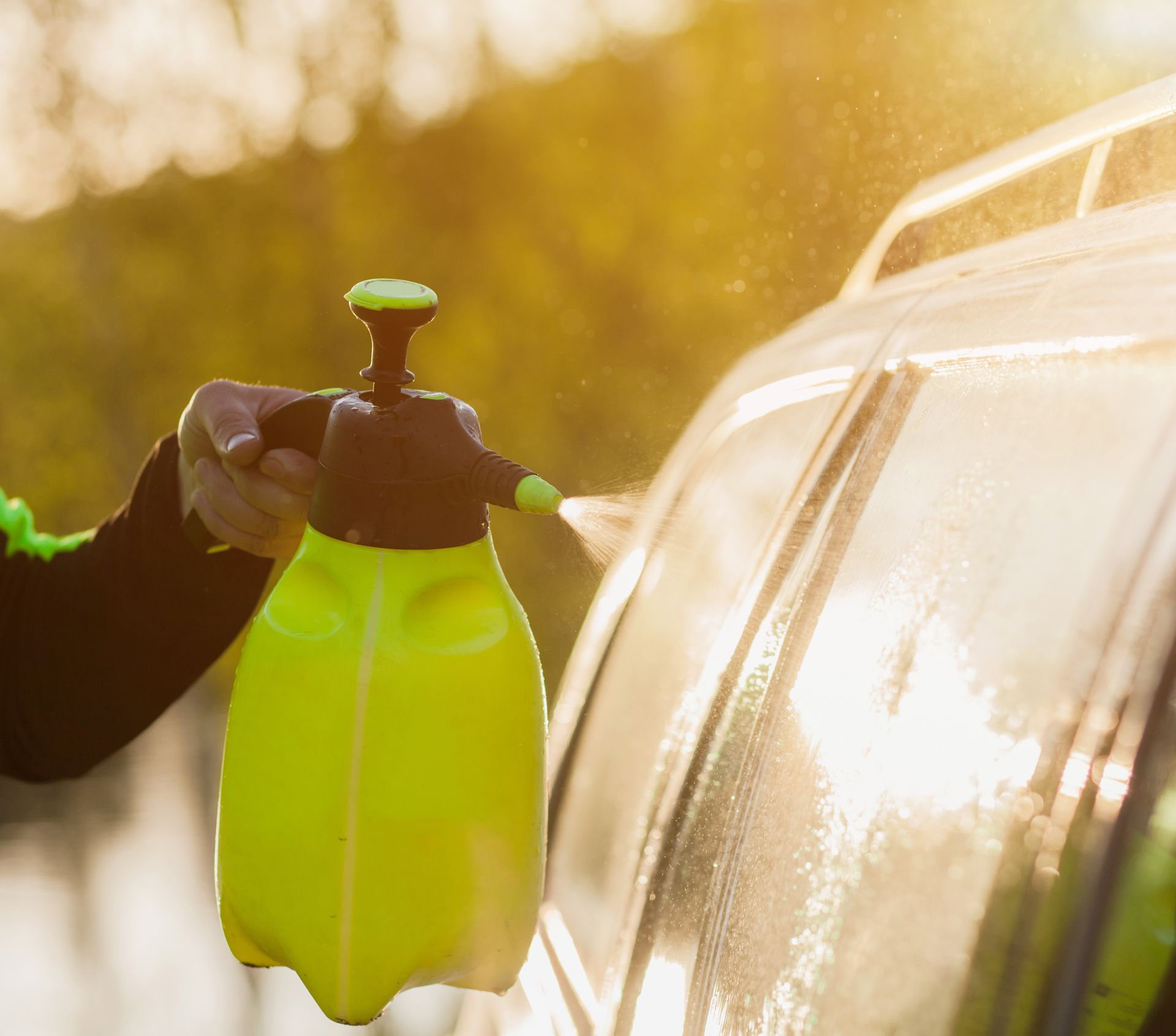 A person is spraying a car with a yellow spray bottle.