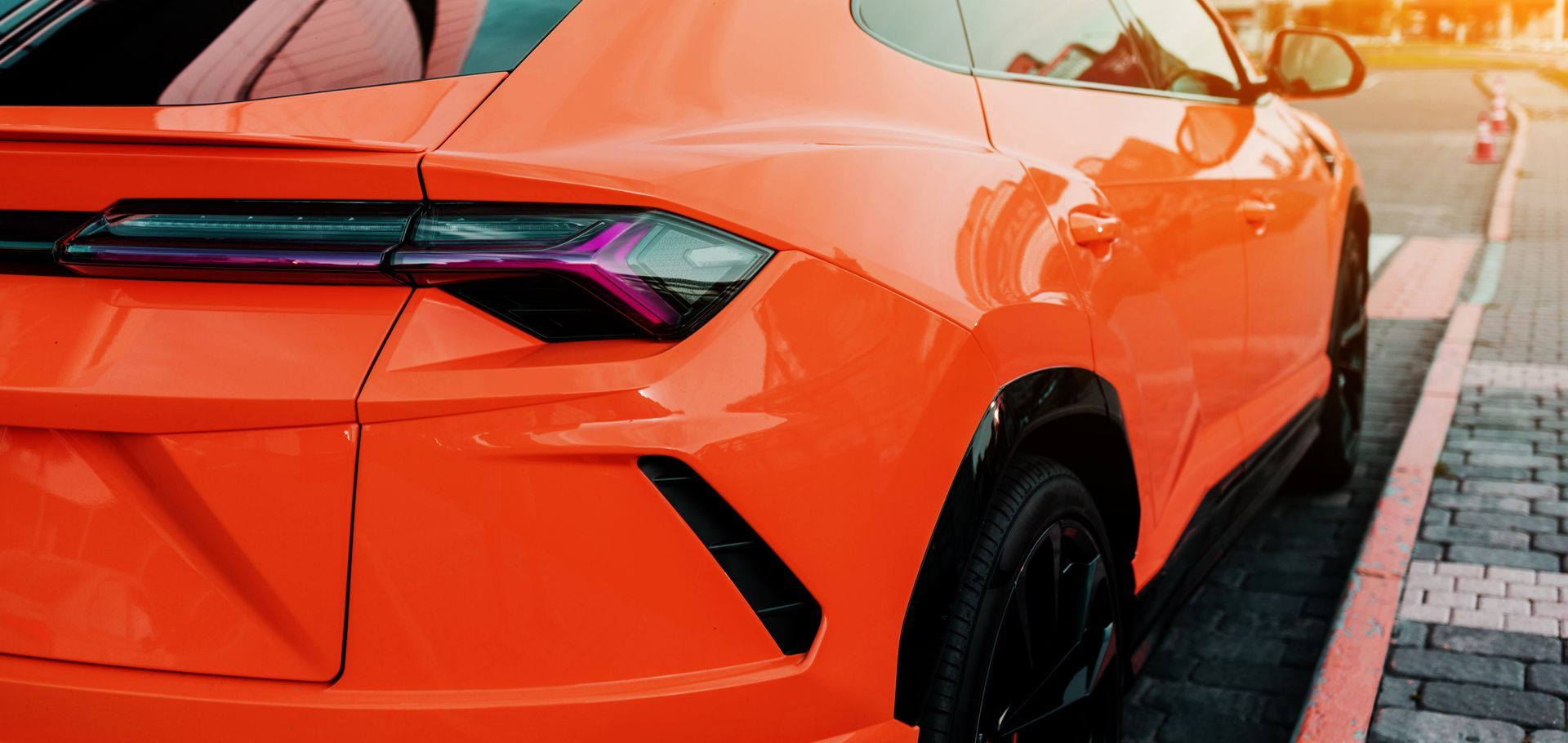 A close up of an orange sports car parked on a sidewalk.