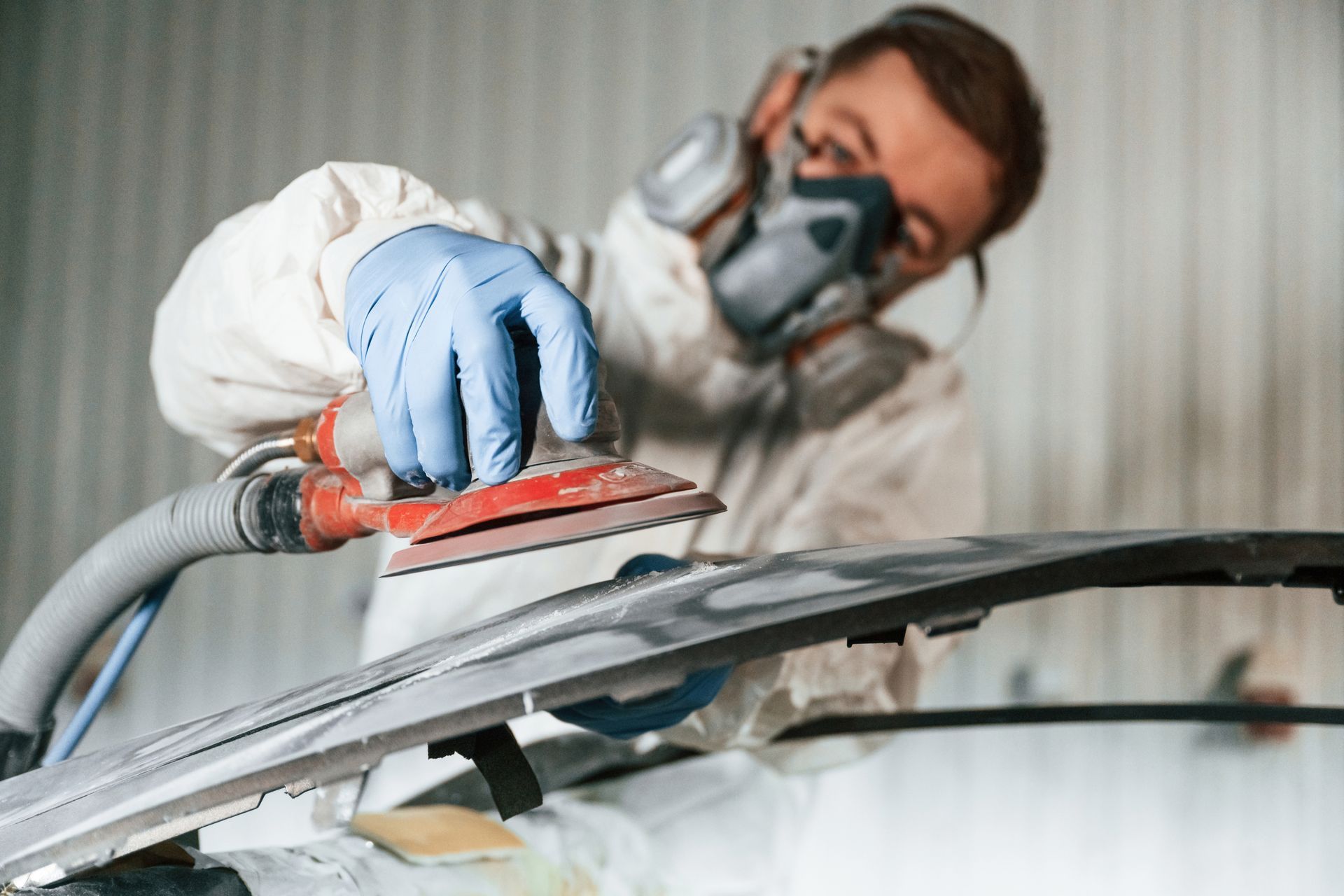 A man wearing a mask and gloves is sanding a piece of metal.