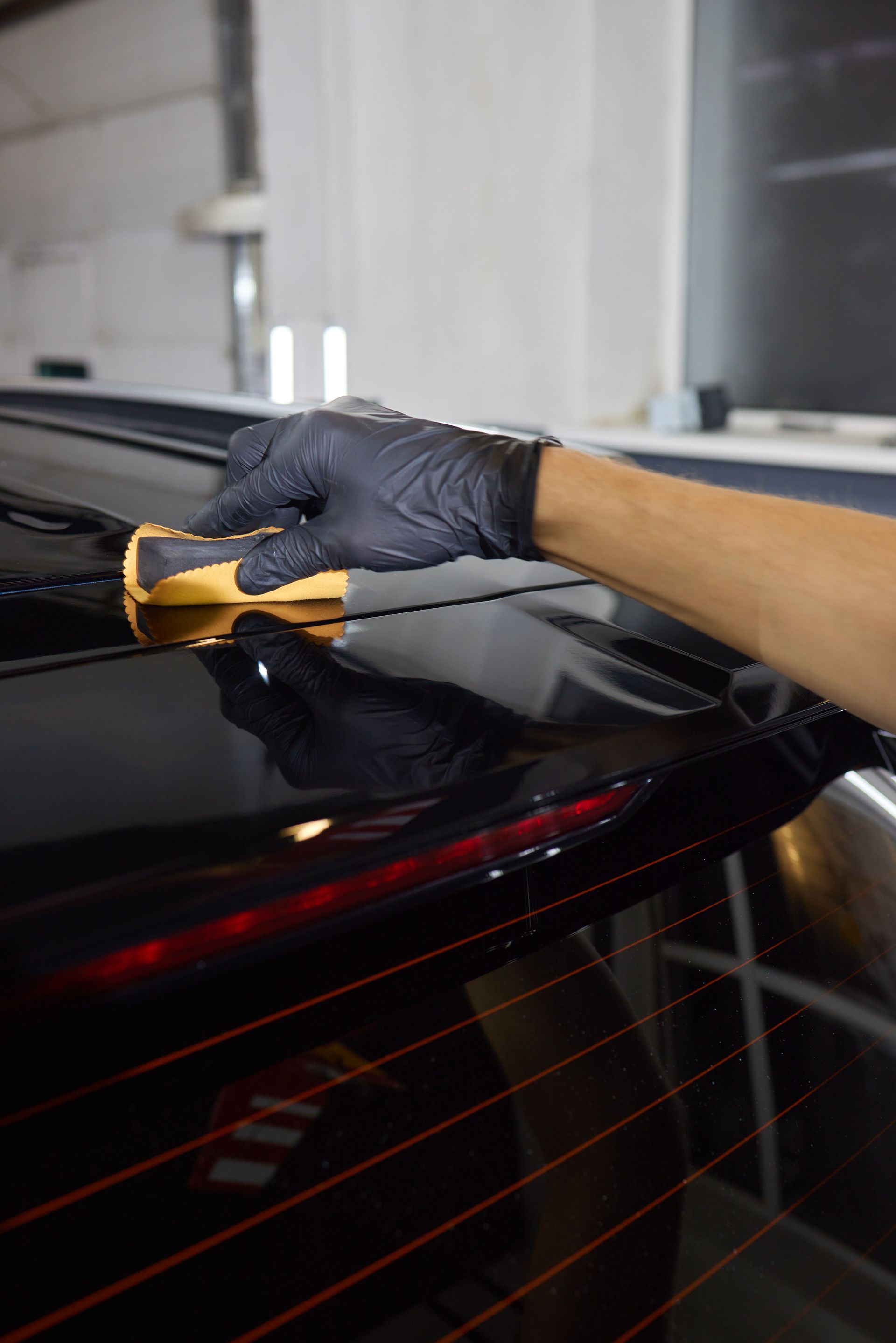 A person wearing black gloves is cleaning a black car with a cloth.