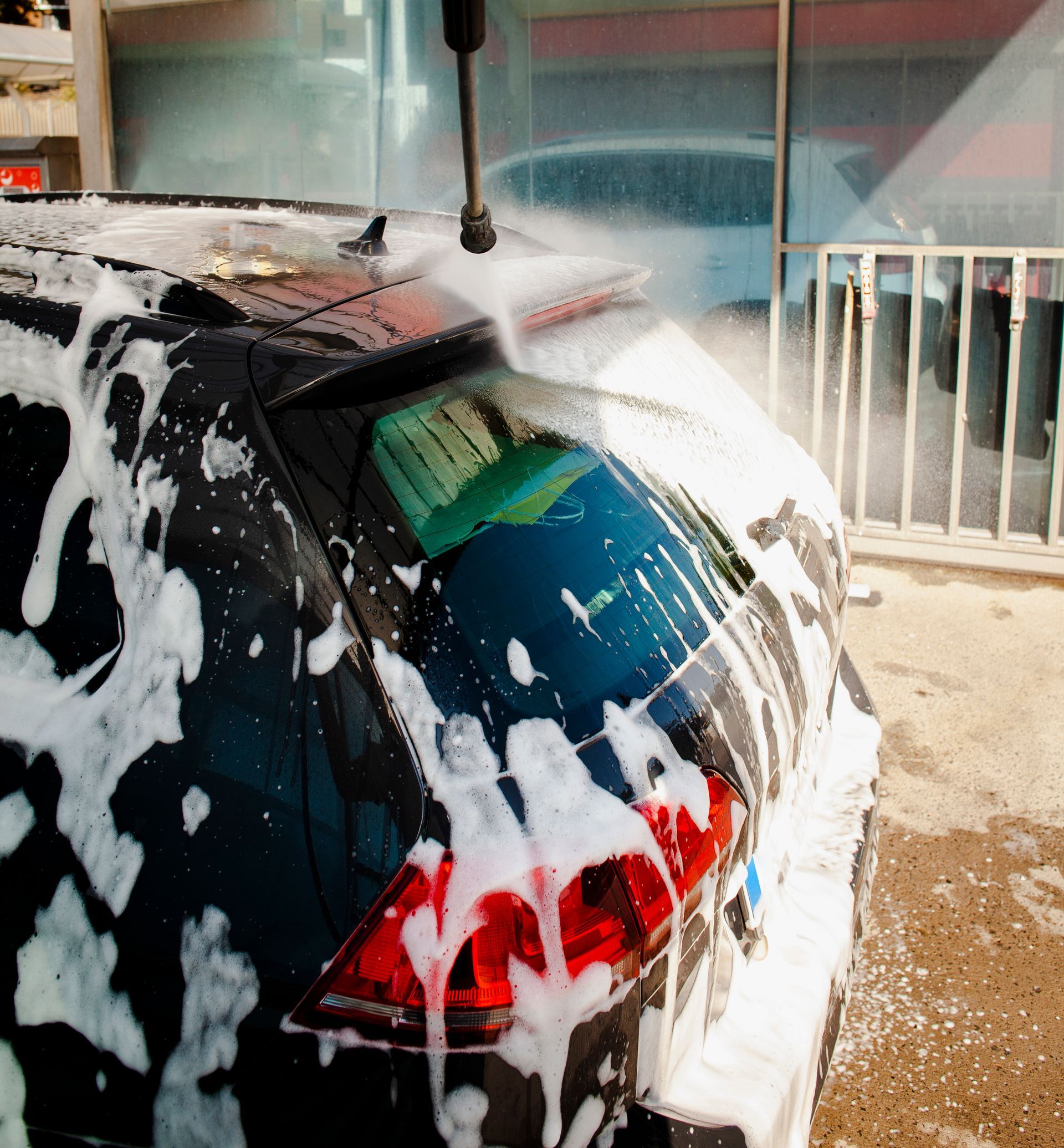 A car covered in foam is being cleaned by a high pressure washer