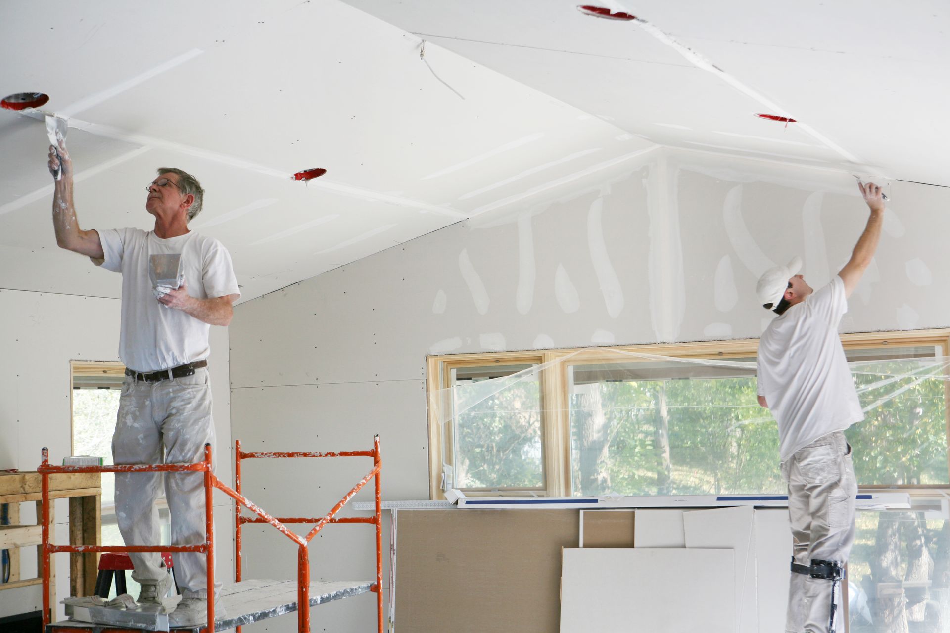 Two men are painting the ceiling of a house