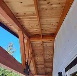 The ceiling of a porch with wooden beams and a wooden roof.