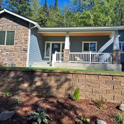 A small house with a porch and a brick wall in front of it.