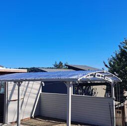A carport with a blue roof is in front of a house.