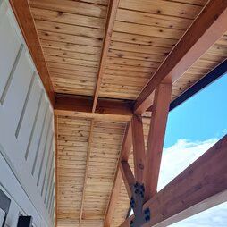 The ceiling of a building with wooden beams and a blue sky in the background.