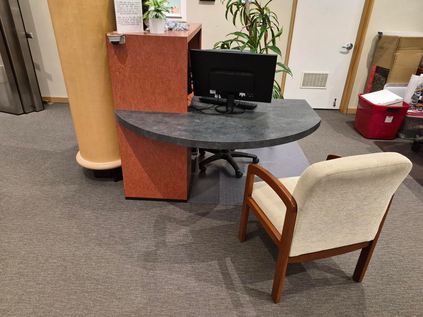 A reception desk with a computer and chair in a room with gray carpet.
