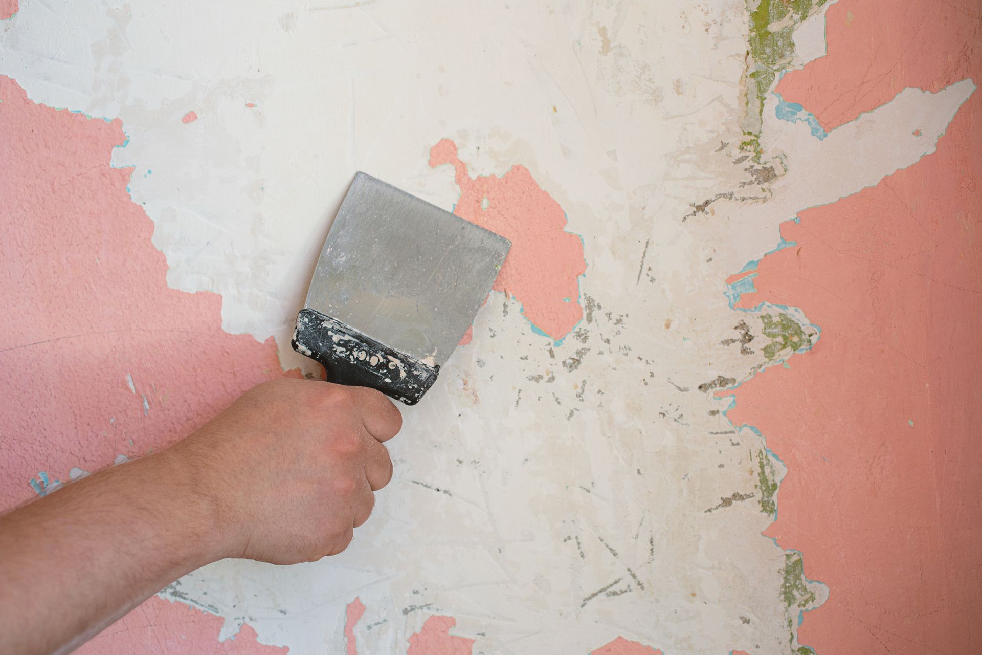 A person is using a spatula to remove wallpaper from a wall.